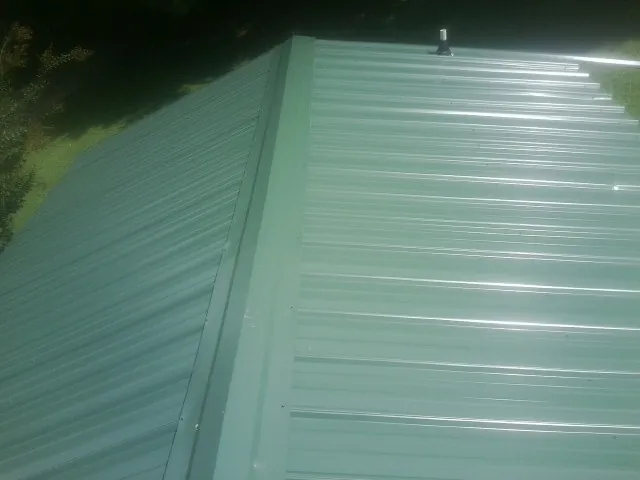 New green metal panels meeting at the ridge of a roof — Flat Roof Repair work by our crew in Houston