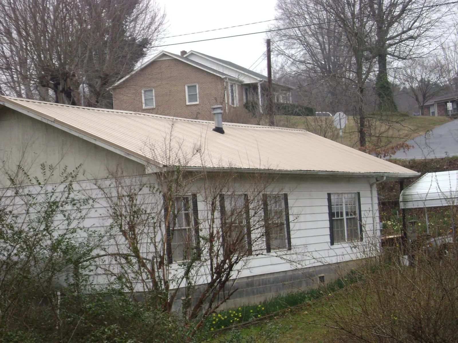 Tan metal roof on a white sided house set into a hillside — Commercial Roofing by Roofing Brothers in Houston